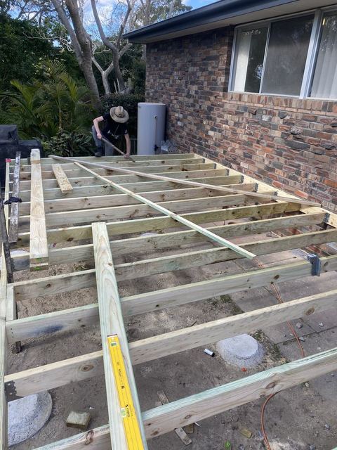 Deck frame of treated pine joists set out beside a brick house